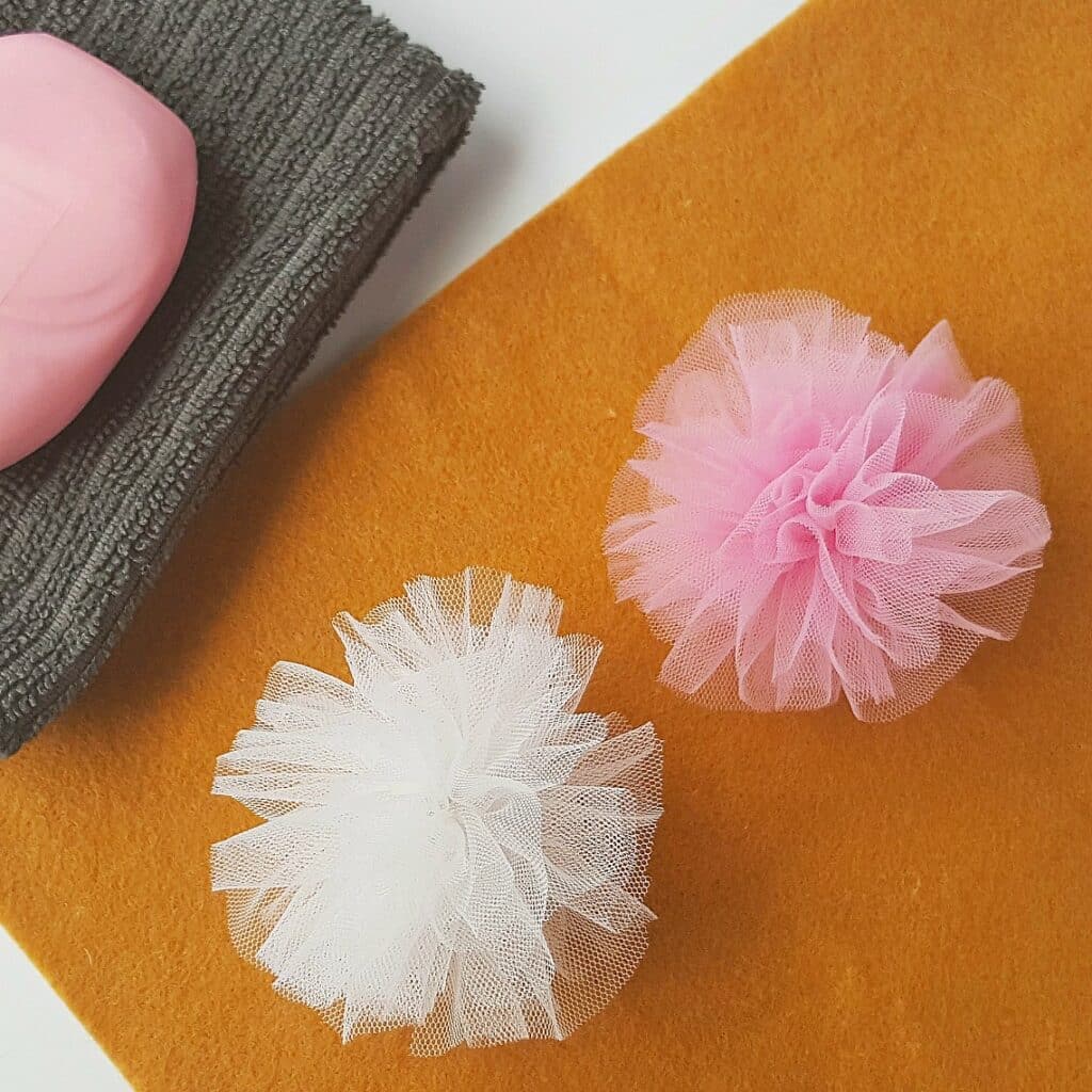 white and pink bath scrubbies on yellow felt against grey washcloth with pink soap bar