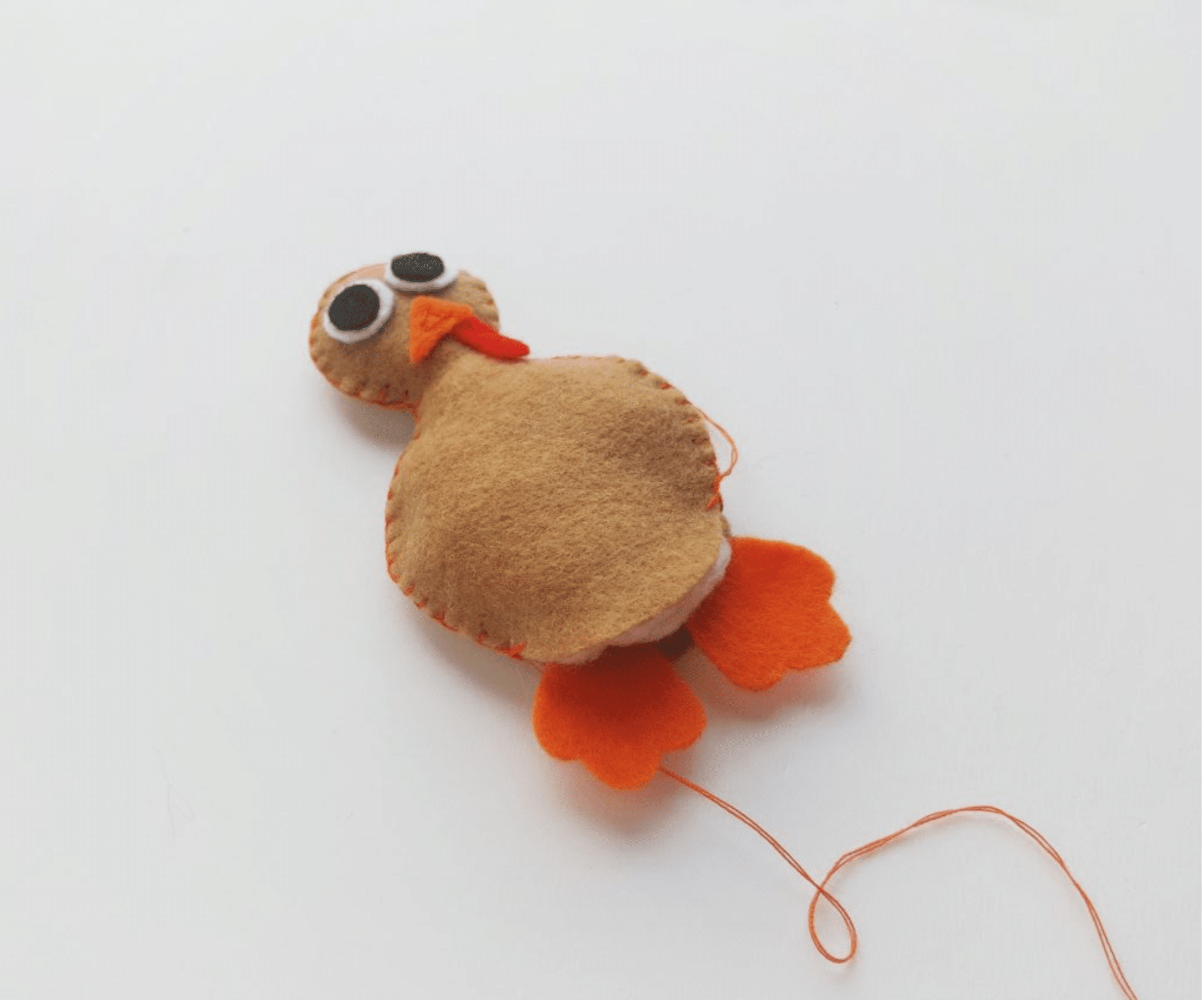 A handmade felt turkey craft with orange stitched details and googly eyes, positioned on a white background with some loose thread visible.