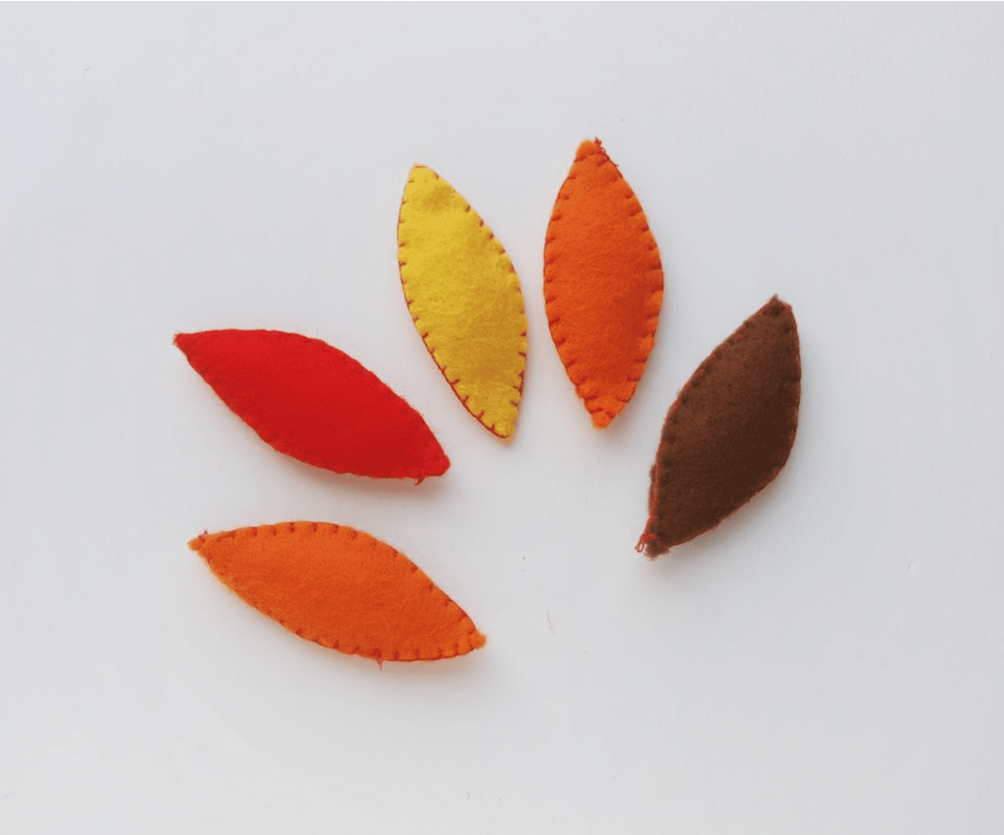 Five fabric leaves in red, yellow, orange, and brown are artfully arranged in a circular pattern on a white background, perfect for a festive turkey craft.