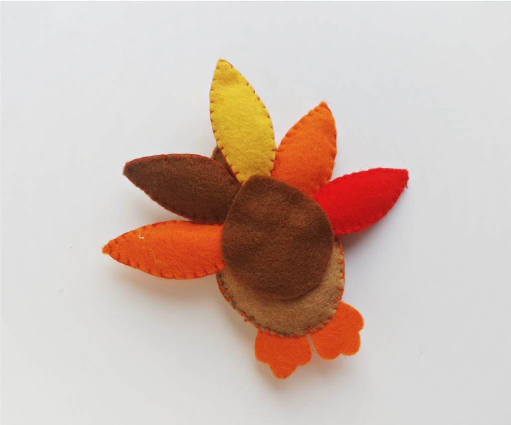 A handmade turkey craft featuring a felt design with colorful feathers in shades of red, orange, yellow, and brown.