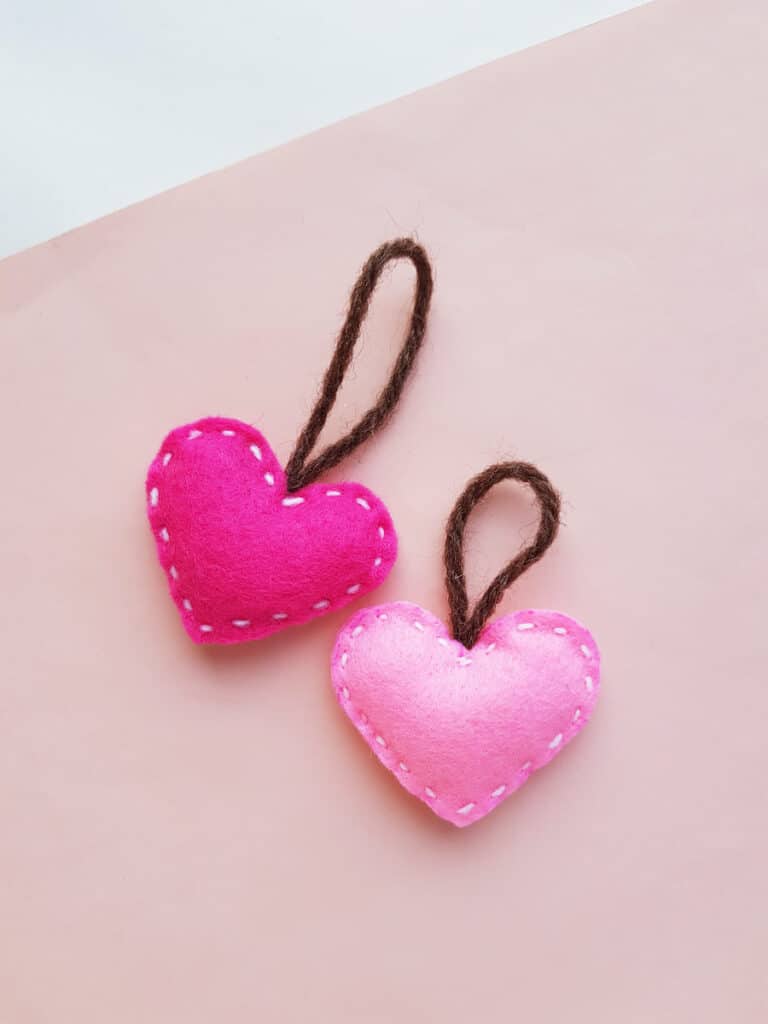 two stuffed felt heart ornaments on pink background