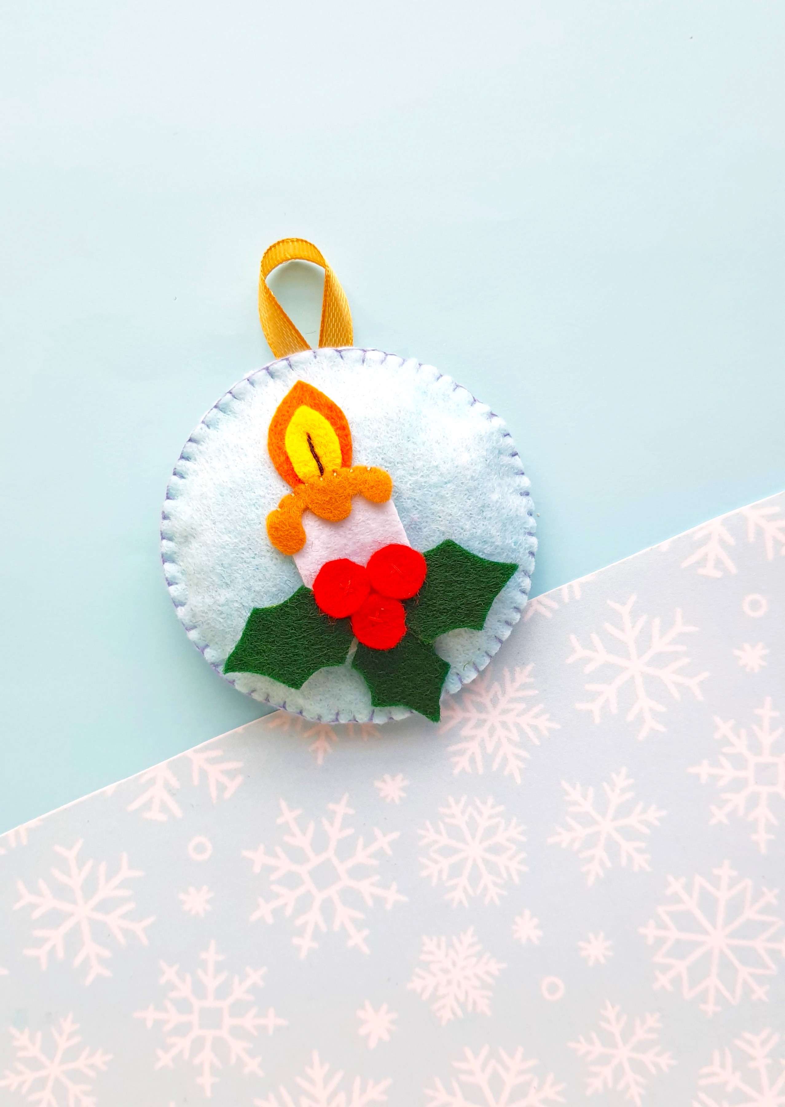 handmade felt candle ornament on a blue and snowflake background 