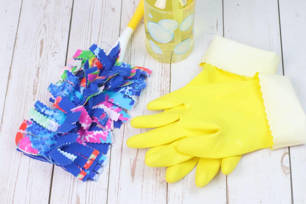 A pair of yellow gloves and a duster on a wooden table.