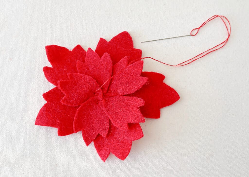 A red felt flower with a needle and thread.