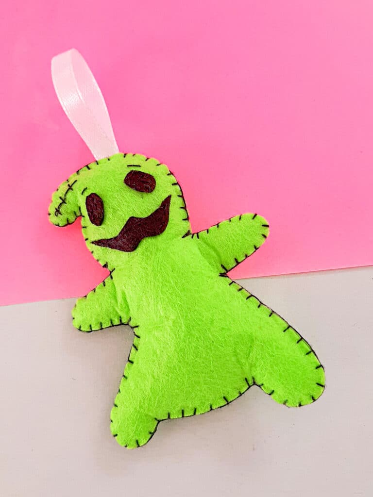 A green felt ghost hanging on a pink background.