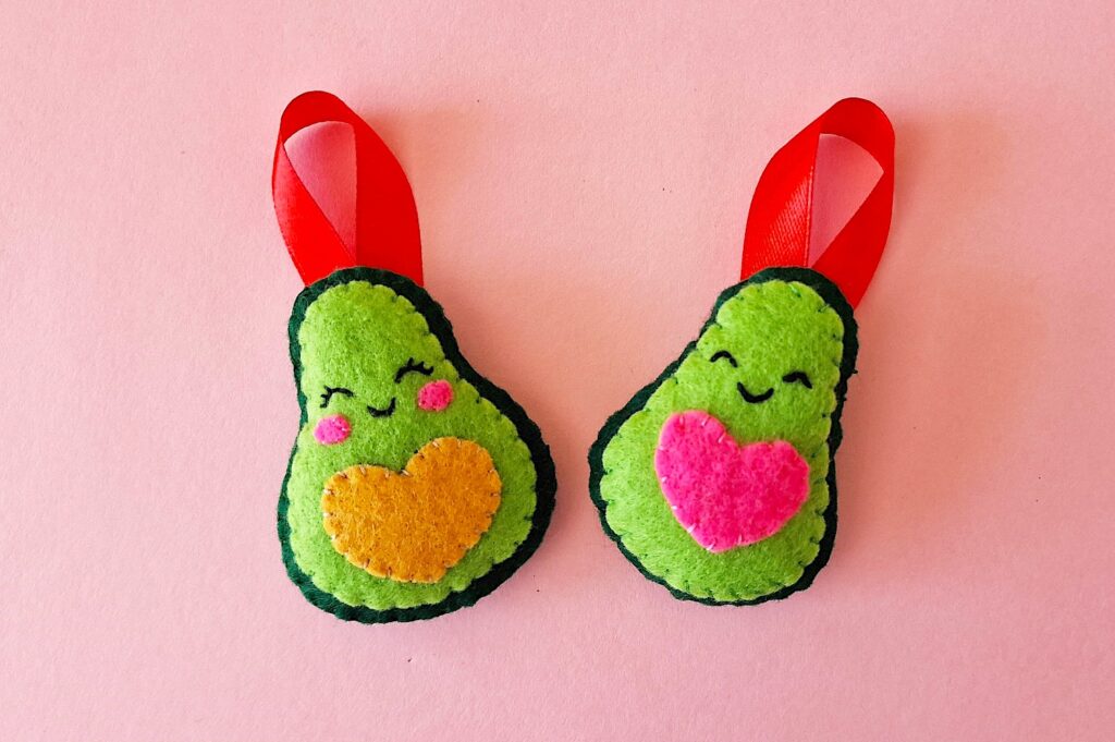 Two felt avocado ornaments on a pink background.