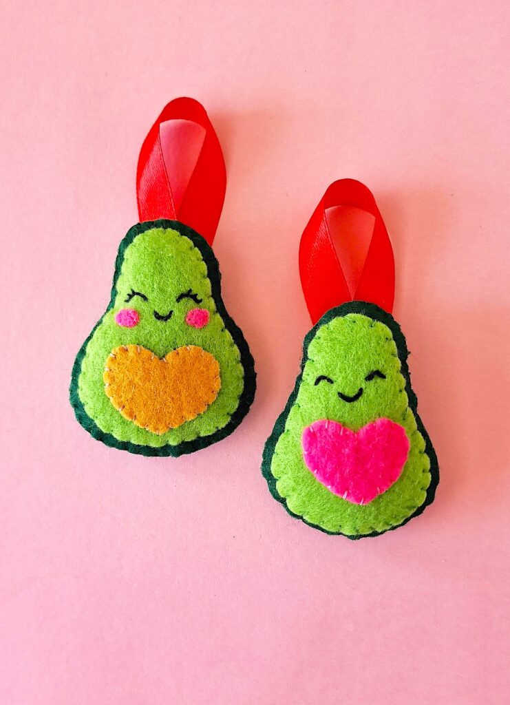 A pair of felt avocados on a pink background.