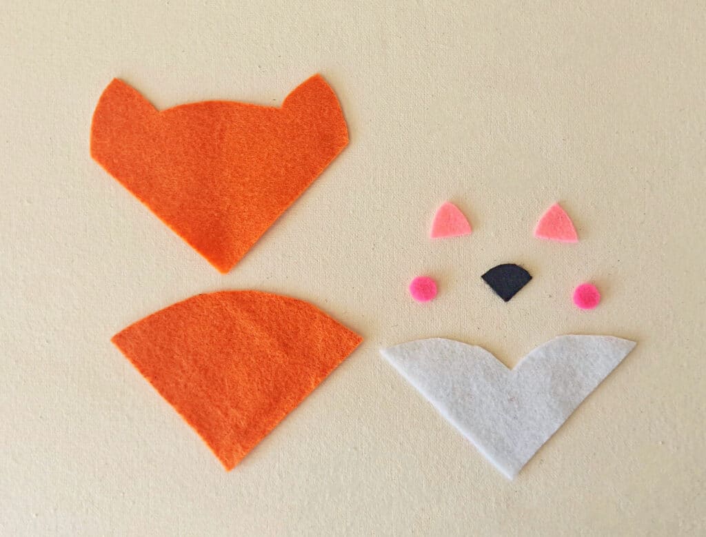 A felt fox and a felt owl are laying on top of each other.