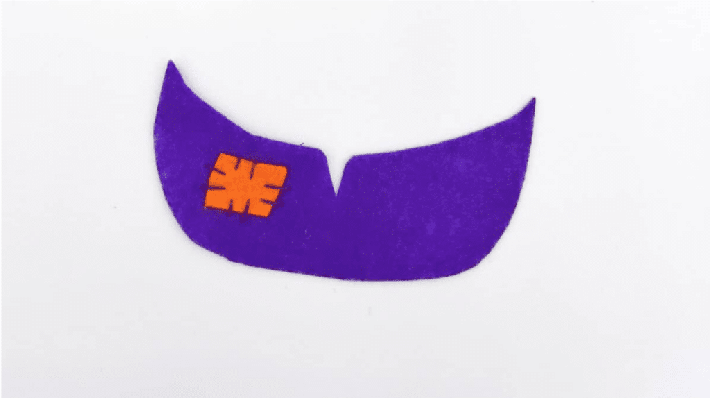 A purple and orange felt Frankenstein candy pouch is on a white surface.