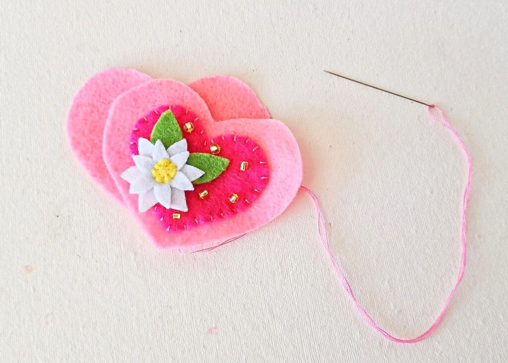 A felt heart with a flower and a needle.