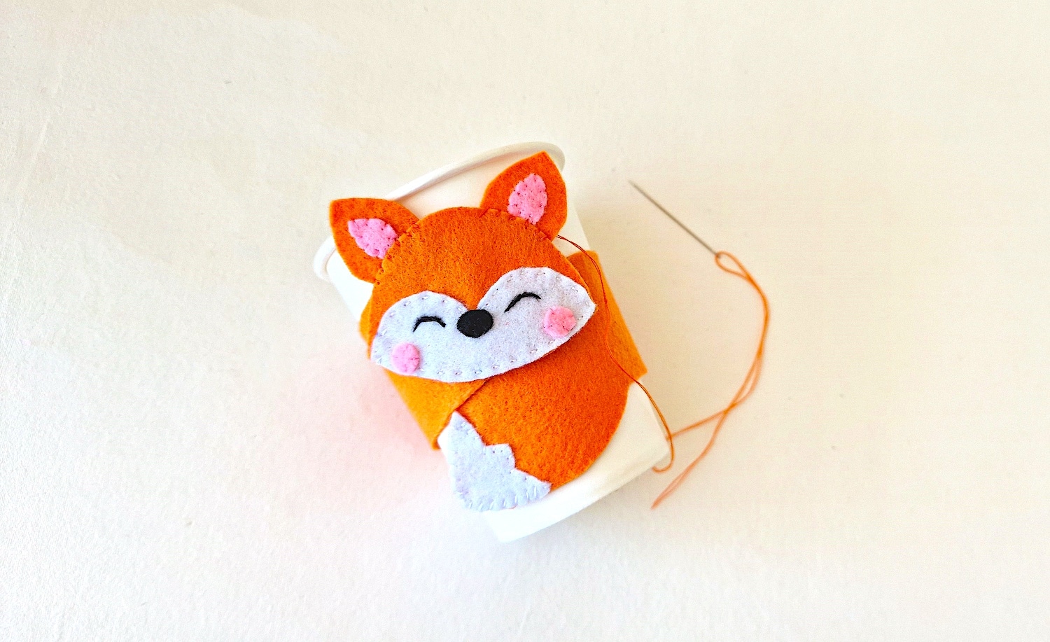 Fox Cup Cozy Step 9 with needle and thread on white background