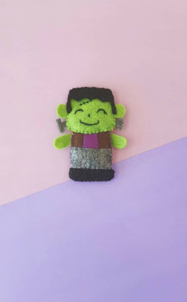 A green frankenstein doll on a pink and purple background.