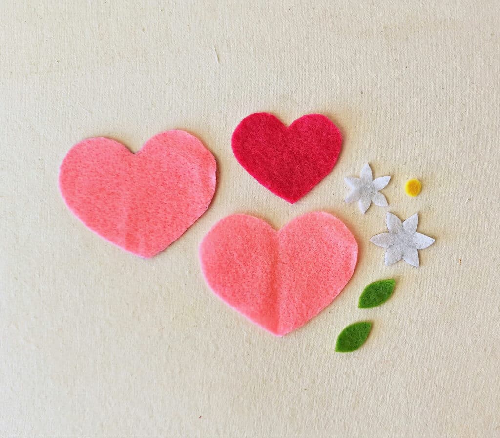 Three felt hearts with flowers and leaves on a table.