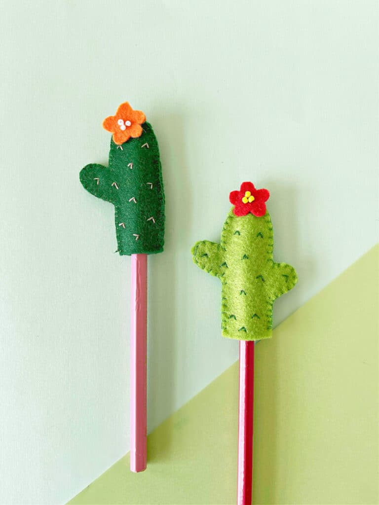 Two felt cactus pencil toppers with flowers on them.