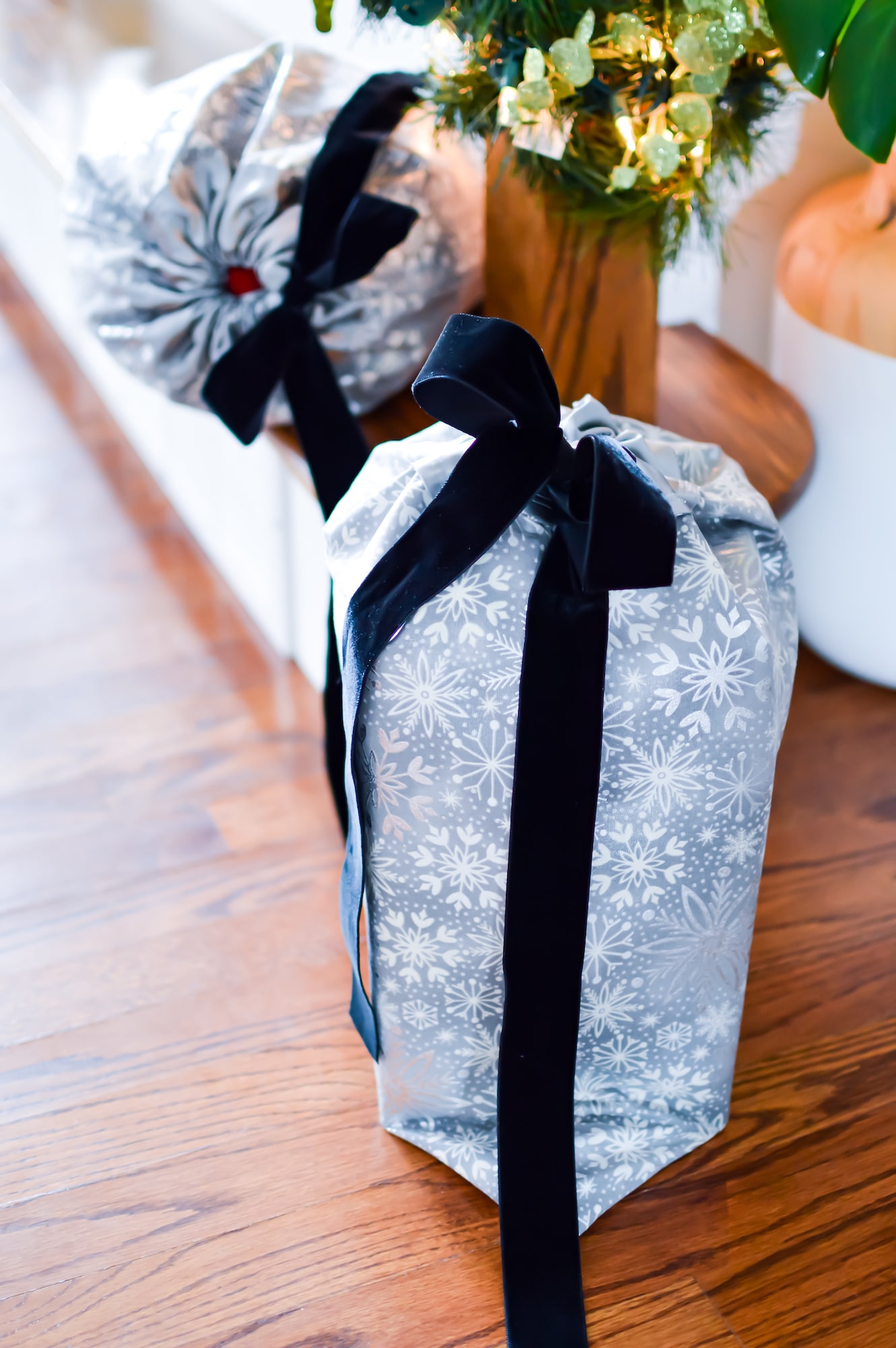Two gift bags on a wooden floor next to a christmas tree.