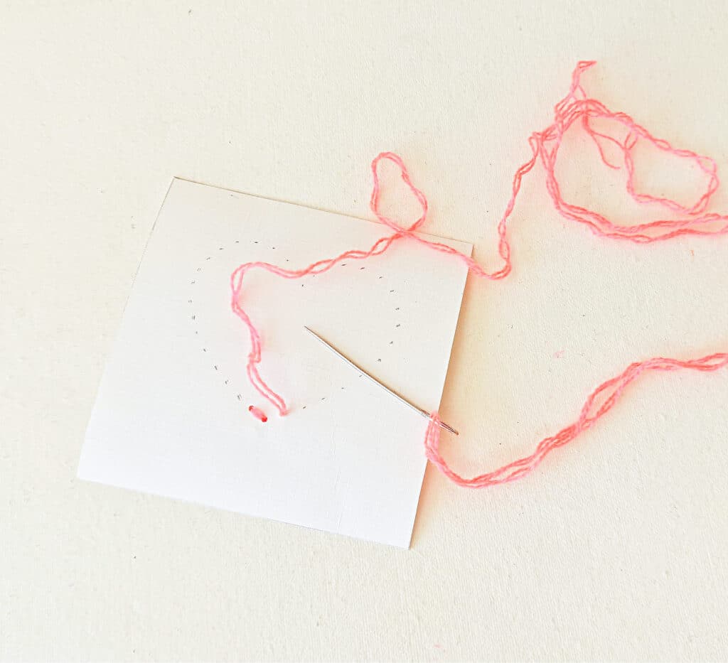 A piece of paper with pink thread and a needle.