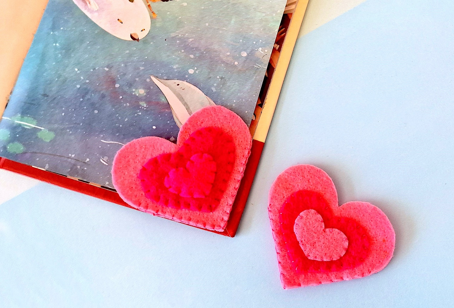 Two felt heart bookmarks on top of a book.