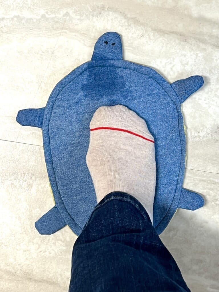 A person's foot on a blue stuffed turtle mop.