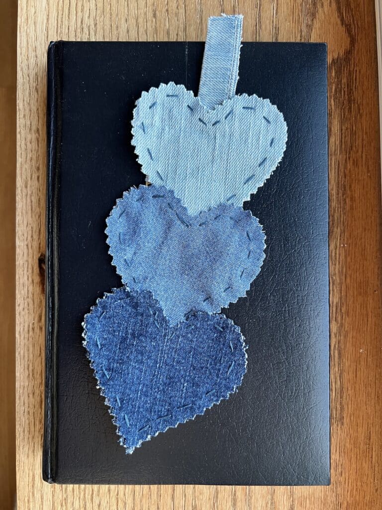 Three stacked denim heart bookmarks on top of a book.