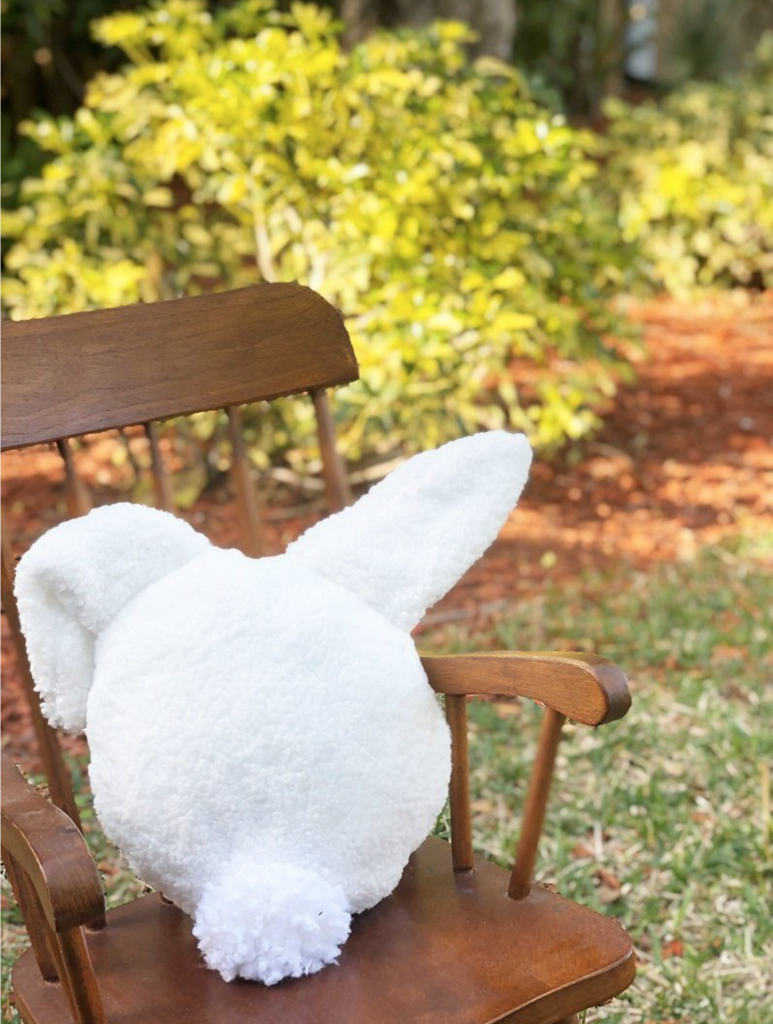 A white bunny pillow sitting on a wooden chair.