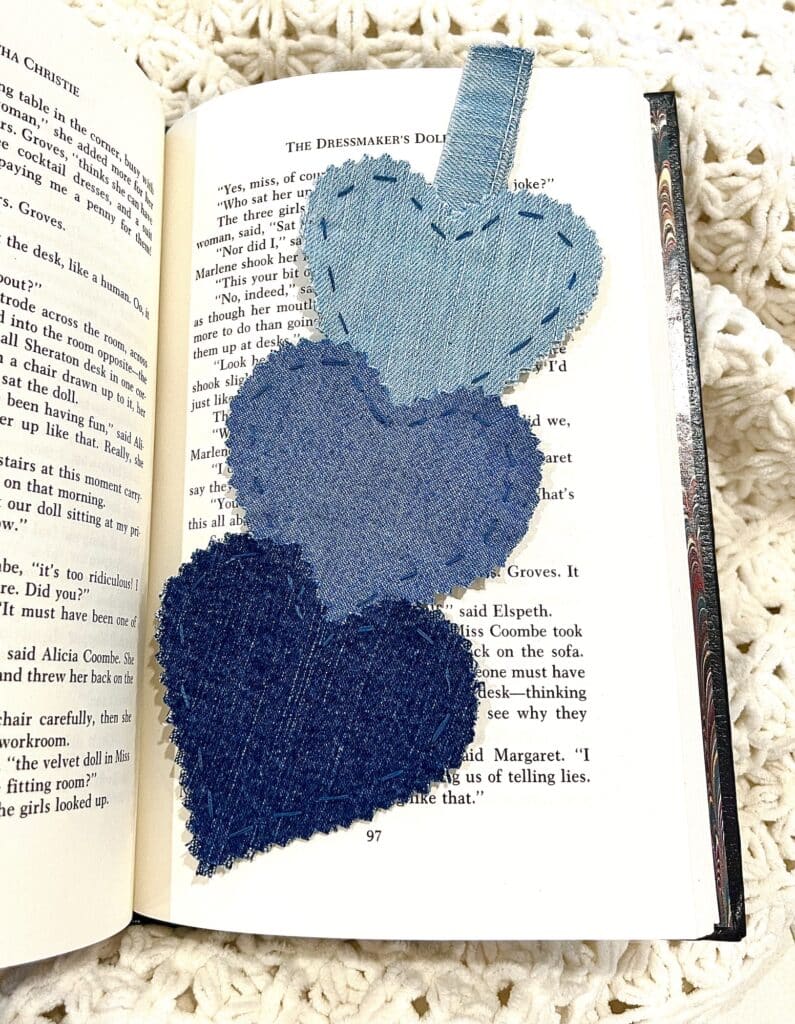 A book with three stacked blue denim heart bookmarks.