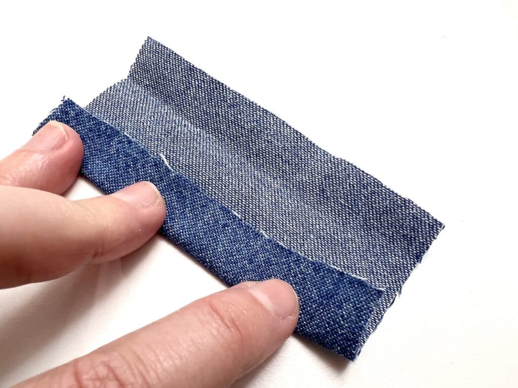 A person's hand holding a piece of denim fabric.