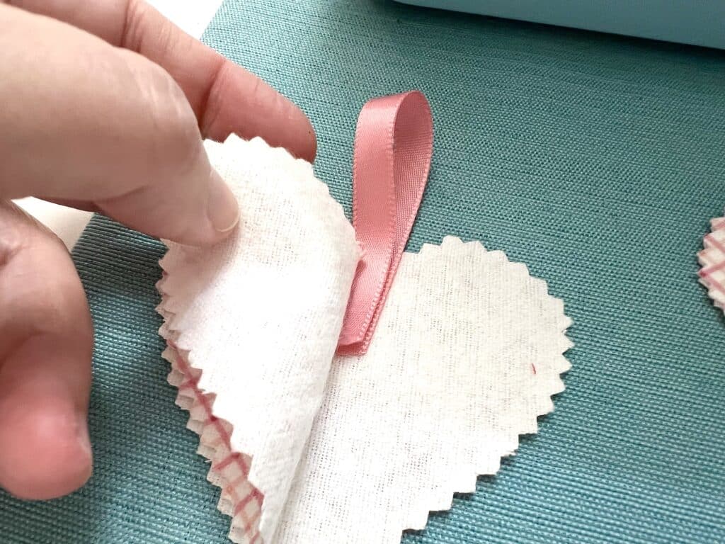 A person carefully cuts a piece of paper into a heart shape, creating a stacked hearts bookmark.