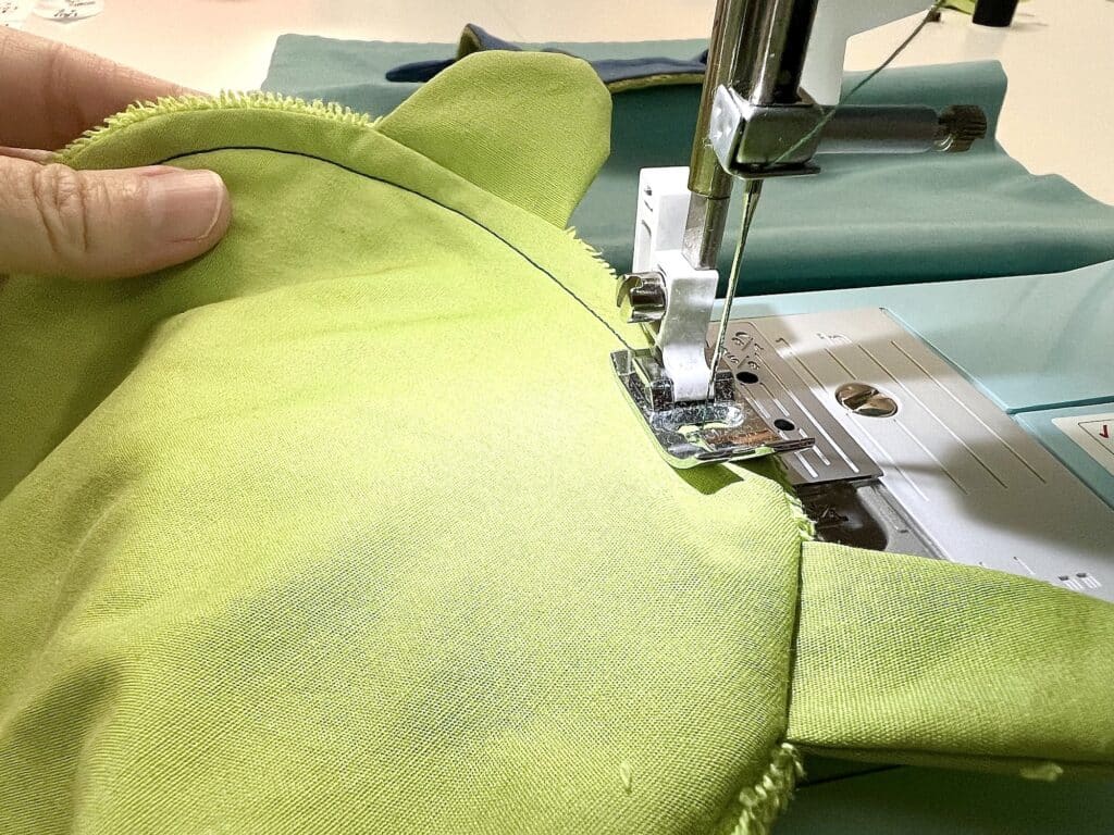 A person sewing a green teddy bear on a sewing machine with the help of a turtle.