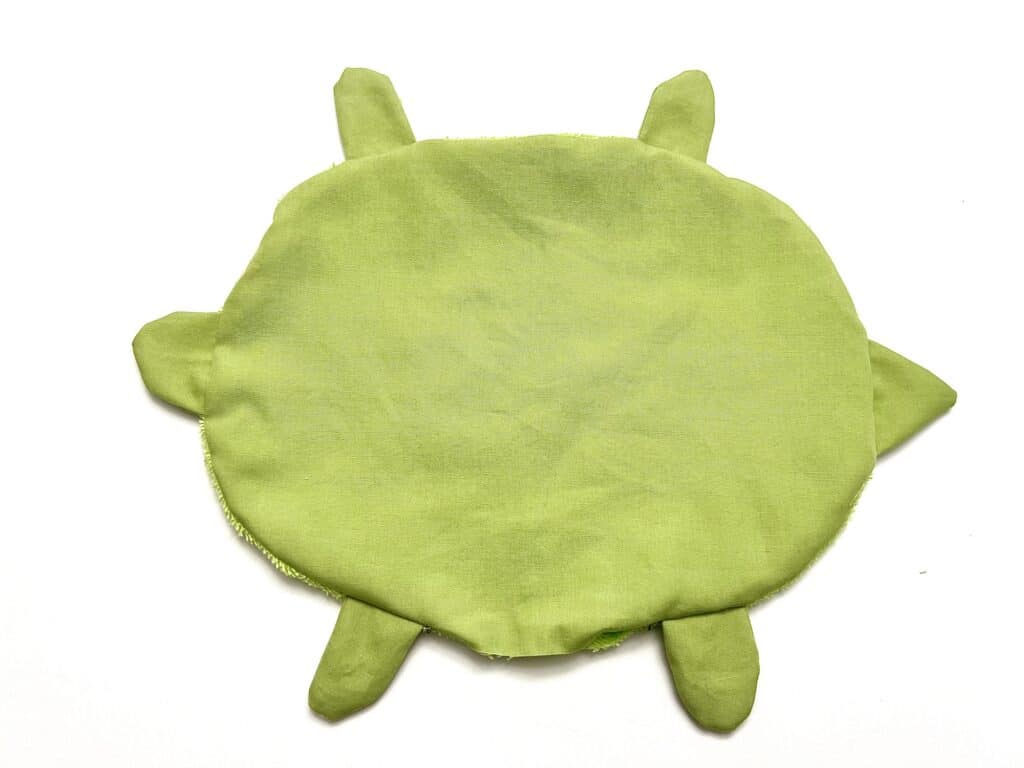 A green turtle shaped pillow on a white surface.