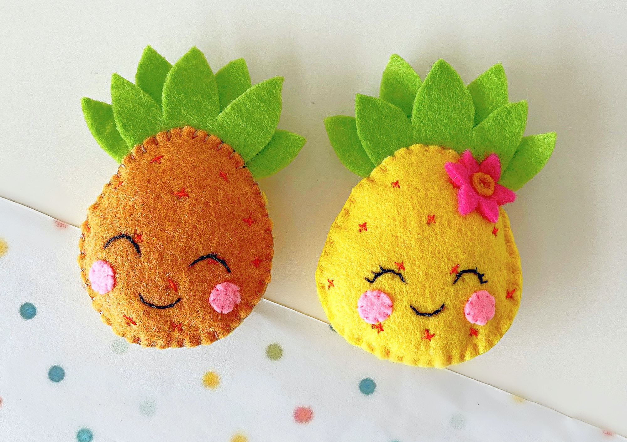 Two pineapple-shaped decorations made of felt on a background adorned with polka dots.