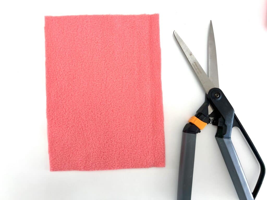 A pair of scissors next to a piece of pink felt.