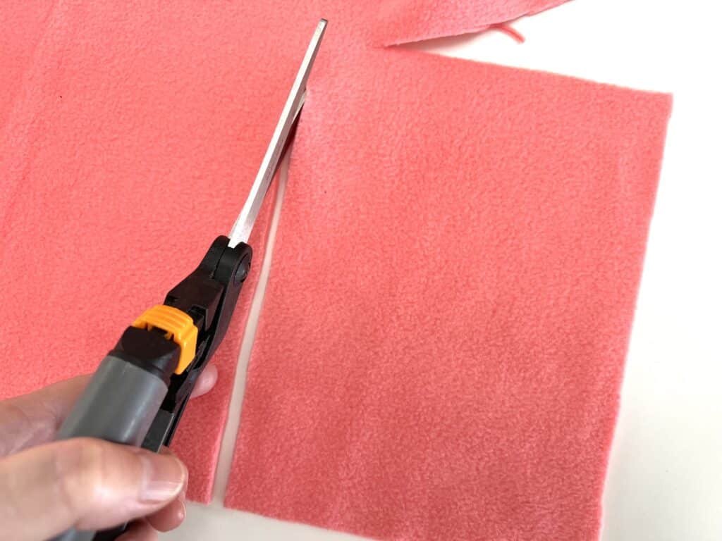 A person cutting a piece of pink felt with scissors.