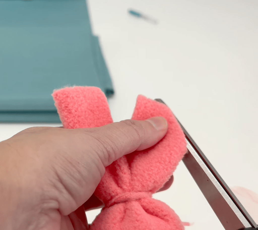 A person cutting a piece of pink felt to make a bunny.
