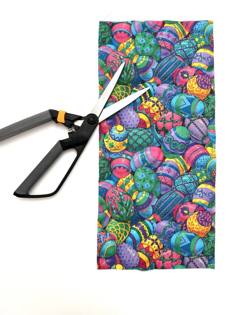 A pair of scissors lying on top of a colorful, crayon-bag-patterned paper.