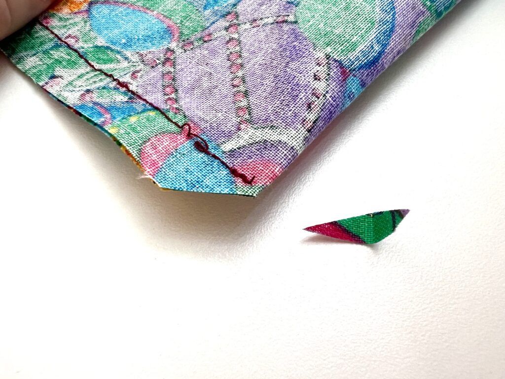 A colorful crayon bag with a matching small triangular scrap on a plain white surface.