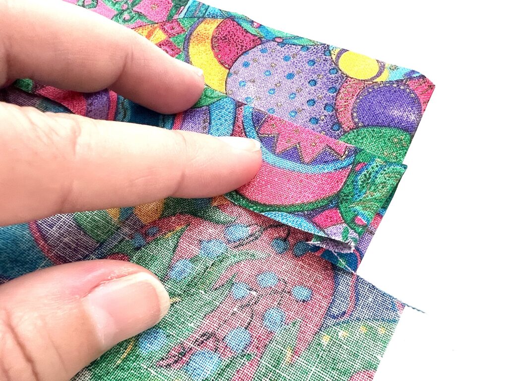 A hand pulling apart layers of colorful, textured crayon bag fabric.