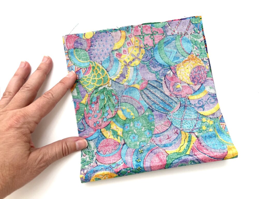 An open fabric-covered crayon bag with a colorful abstract design held by a hand against a white background.