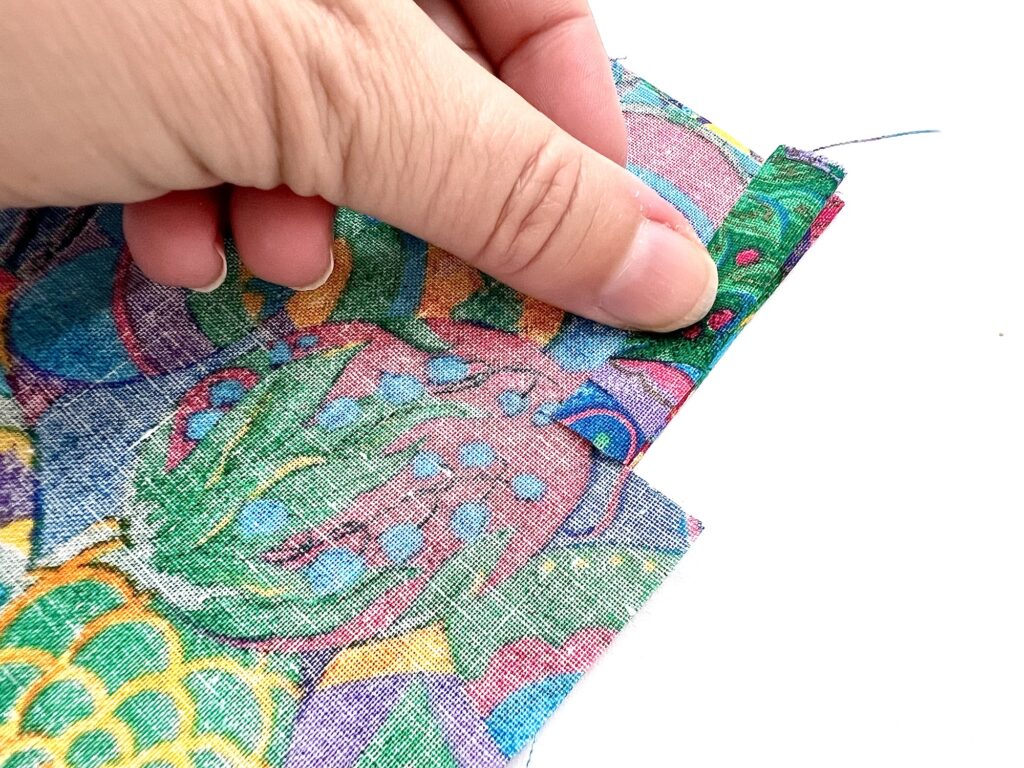 A hand holding a crayon bag made of colorful patterned fabric with a folded hem.