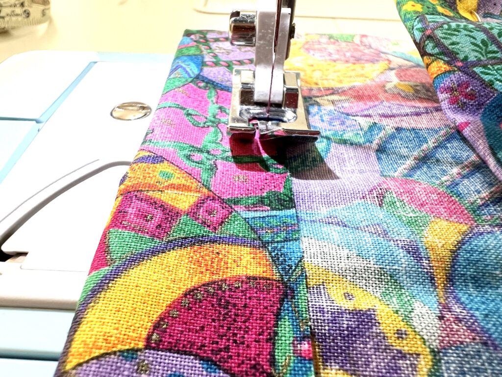 Sewing machine needle and presser foot working on a colorful crayon bag fabric.