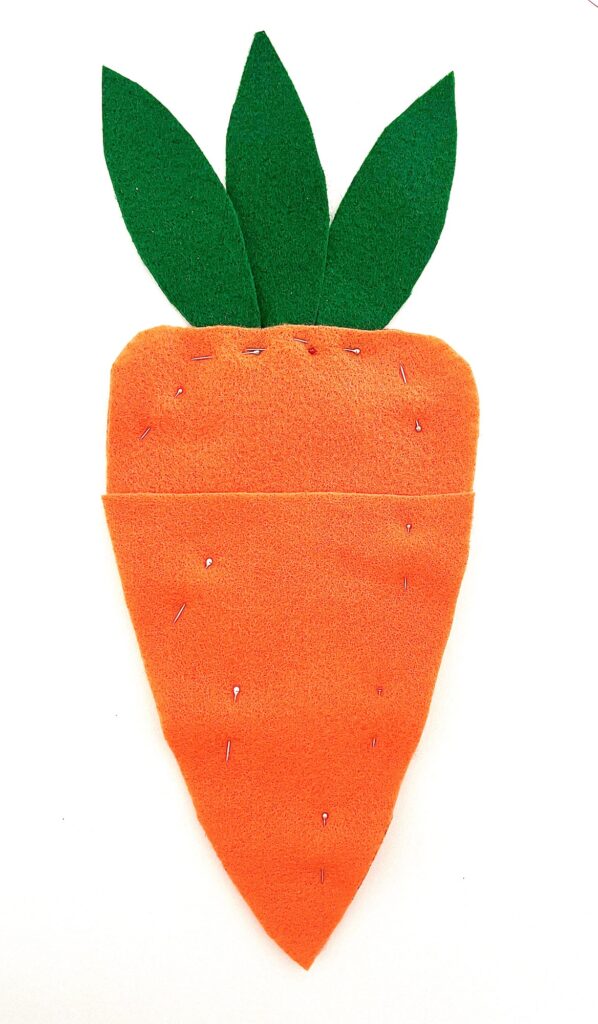 Handcrafted felt carrot with green leaves and a seed packet on a white background.
