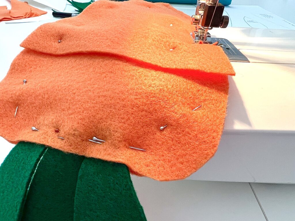 Orange fabric with seed packet pins being sewn on a sewing machine.