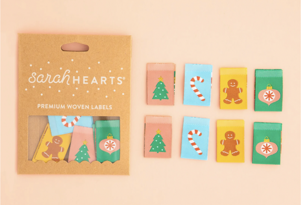 A set of Christmas-themed woven labels featuring a tree, candy cane, gingerbread man, and ornament, with packaging labeled "Sarah Hearts Premium Woven Labels.