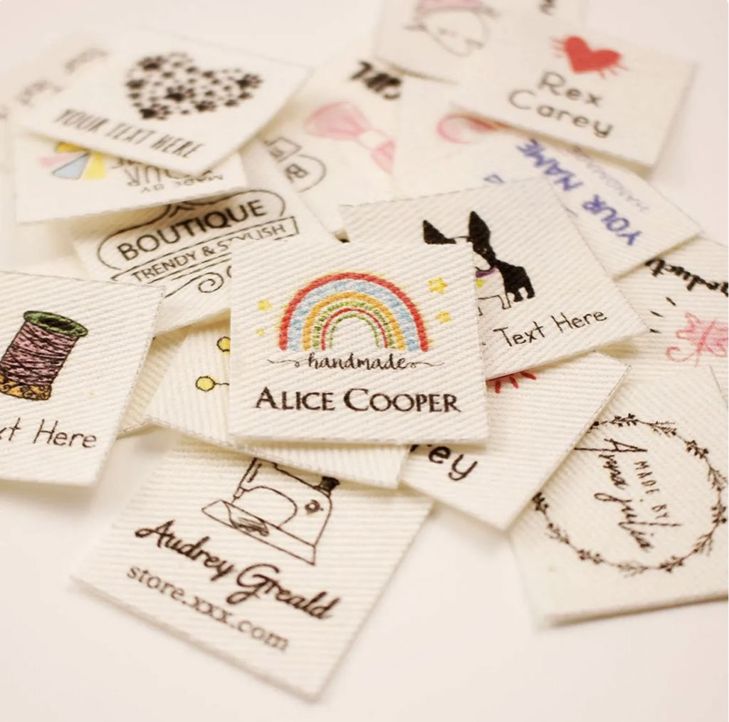 A variety of custom sewing labels on a white surface, featuring different designs, colors, and text styles, including rainbows and animals.