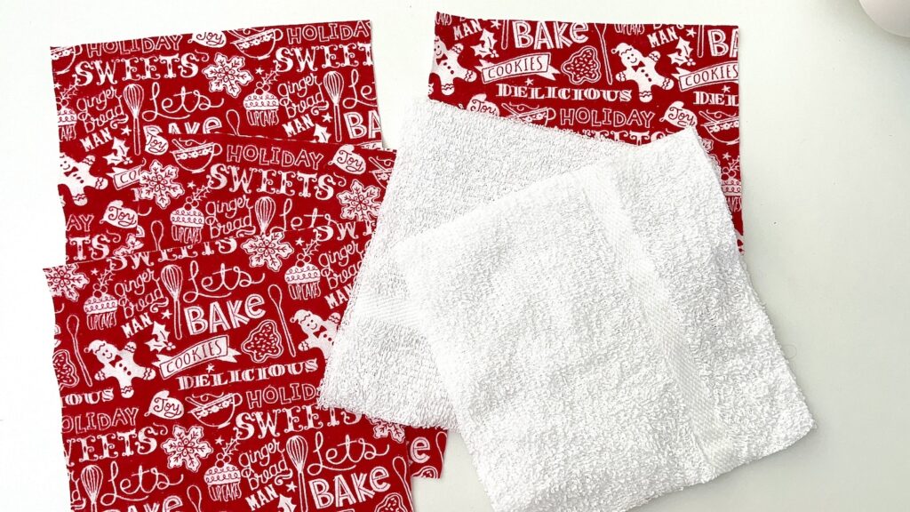 Red and white holiday-themed fabric squares with baking-related text and designs, alongside plain white fabric squares, rest on a white surface. Perfect for crafting festive reusable paper towels.