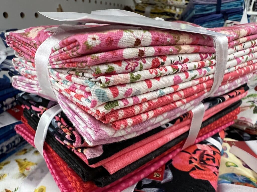 A stack of folded floral and patterned fabrics, tied with ribbons, sits on a shelf.