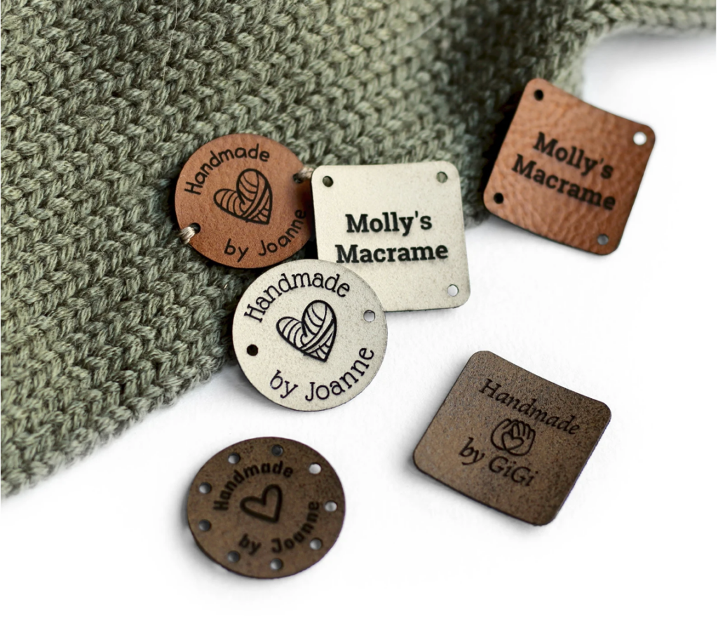 Several engraved wooden labels on a knit fabric, reading "Handmade by Joanne," "Molly's Macrame," and "Handmade by GiGi.