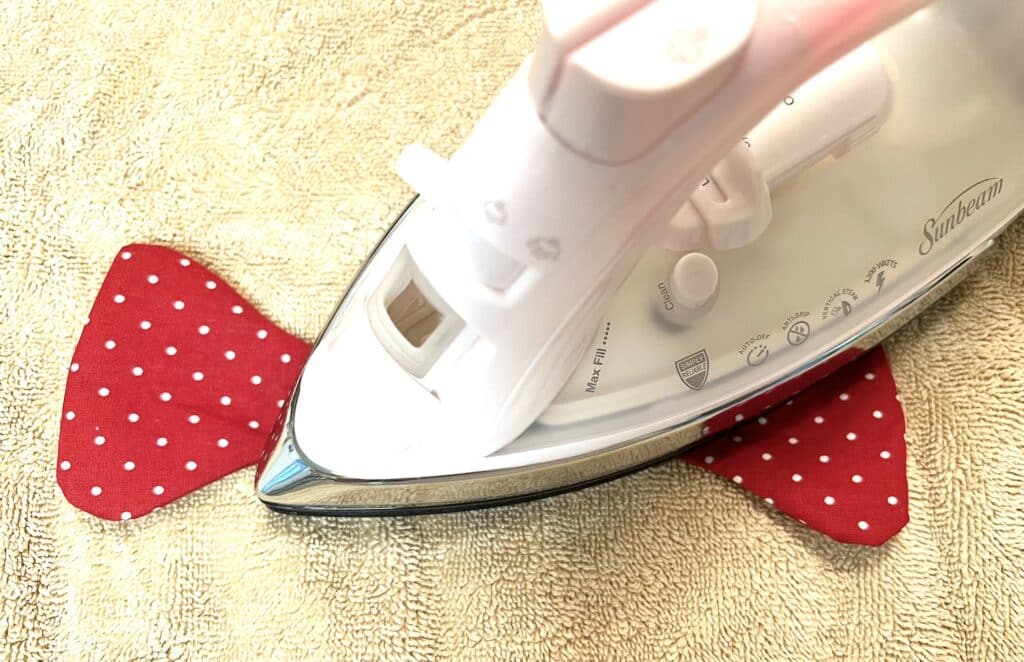 An iron pressing a red polka-dotted fabric on a beige towel.