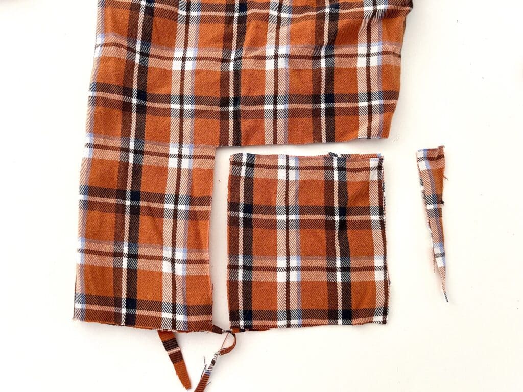 Orange plaid fabric cut into multiple pieces on a white background, perfect for crafting DIY hand warmers to keep you cozy.