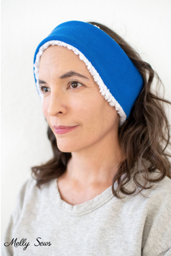 Person wearing a blue and white headband, with medium-length wavy hair, and a light gray top.