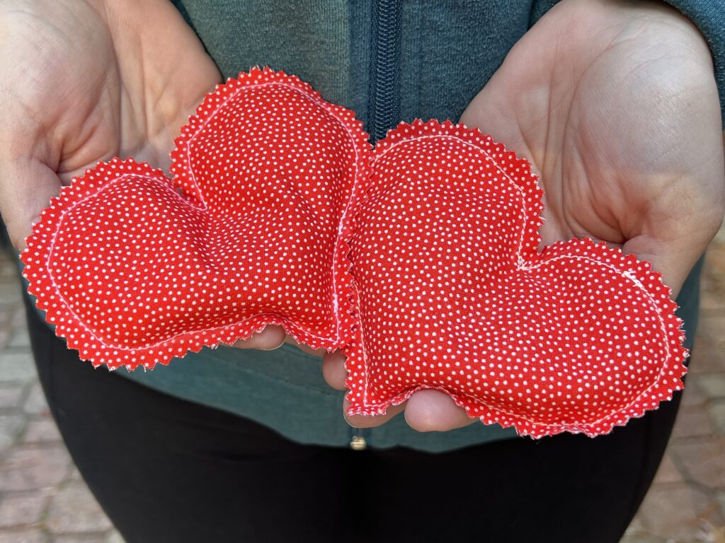 Hands gently cradle two red polka-dot heart-shaped fabric cushions, reminiscent of charming DIY hand warmers.